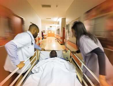 Two medical professionals are pushing a patient in a hospital bed down a hospital hallway.